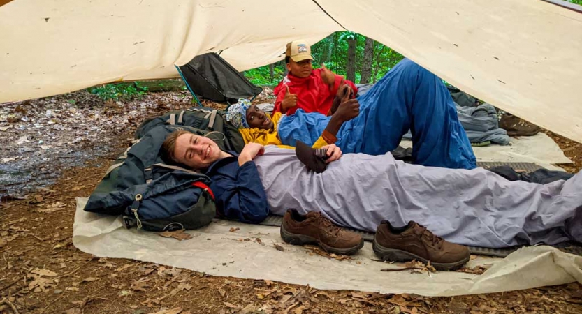 three teens rest under a tarp on an outward bound expedition 